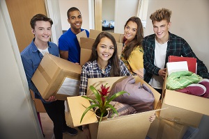 Group of college students in a dorm hallway holding boxes